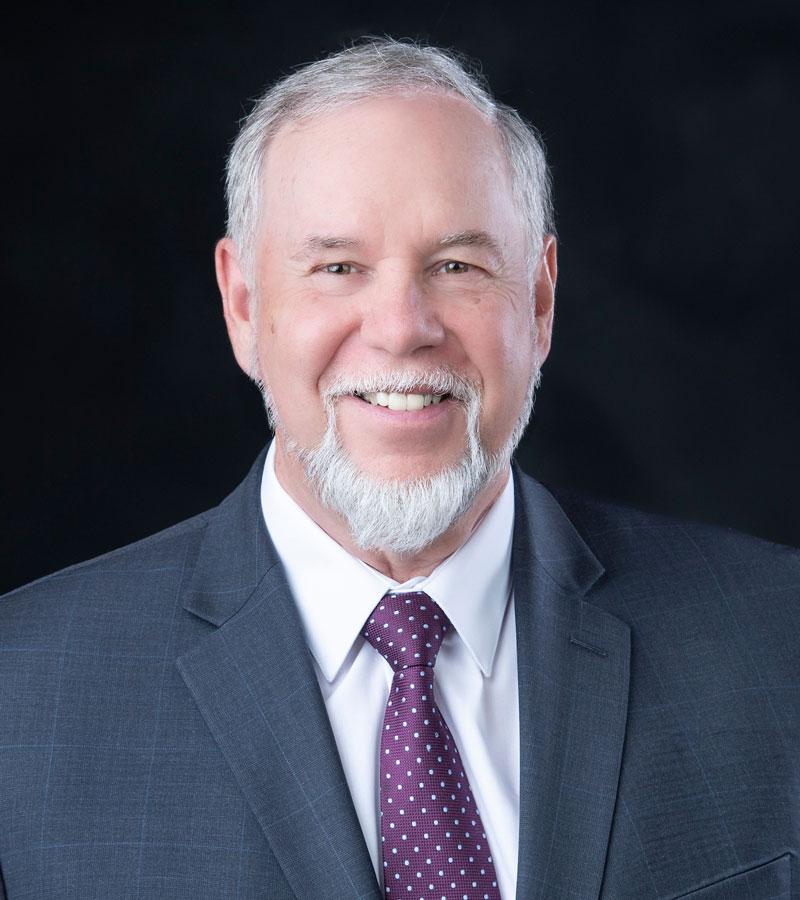 Portrait of Harold Jones, Ph.D. with grey hair and beard wearing a blue blazer, white shirt, and maroon tie.